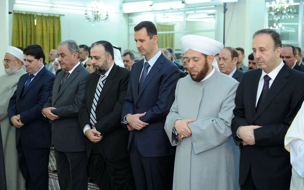 A 2012 image of Assad (center) at Eid al-Fitr prayers at Al-Hamad Mosque in Damascus.