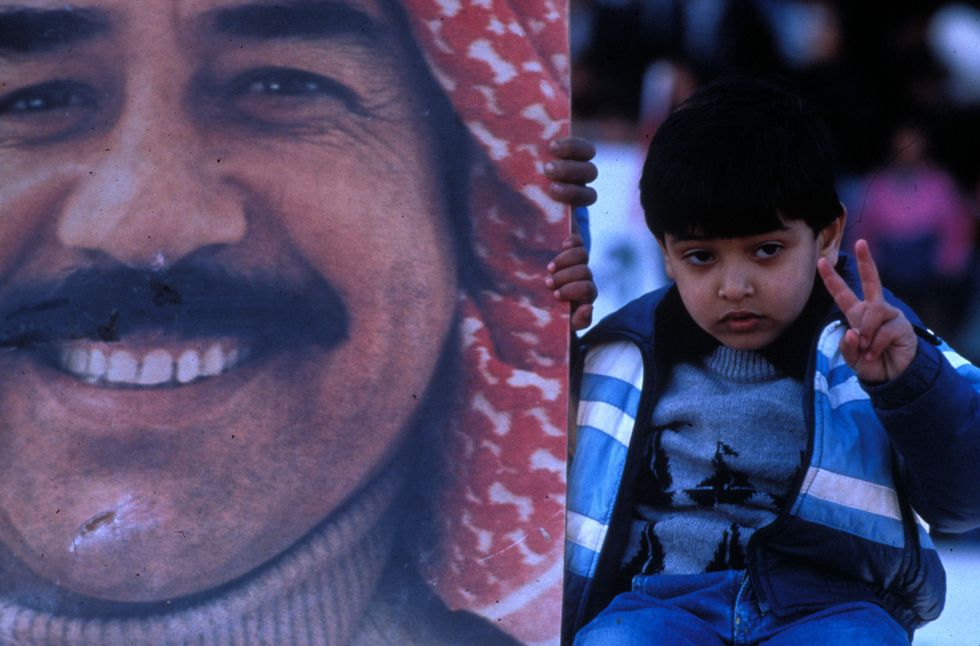 A child poses next to a large poster with Saddam Hussein's face on it