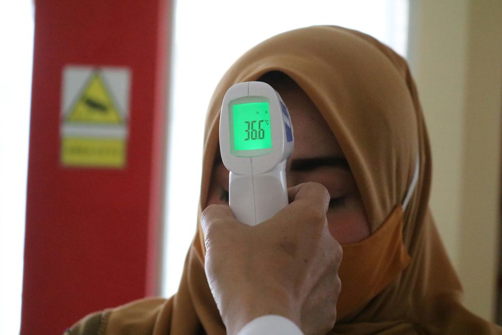 A doctor holds a temperature gauge to a woman's forehead. It reads 36.6 degrees Celsius.