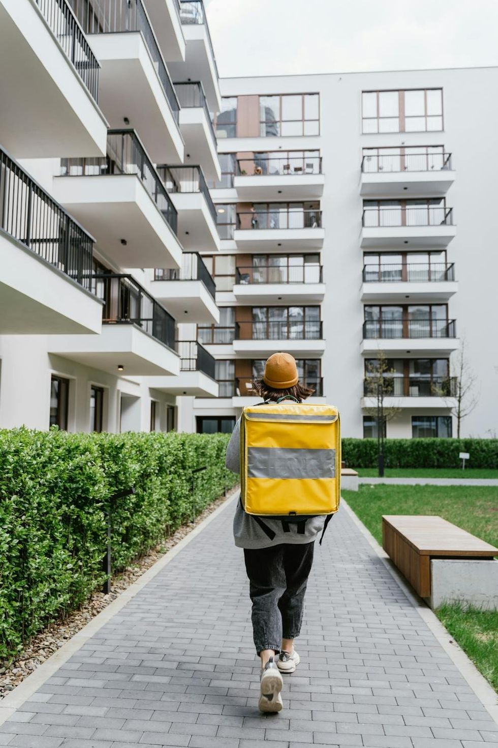 A man carrying a yellow bag walks on a sidewalk near an apartment complex