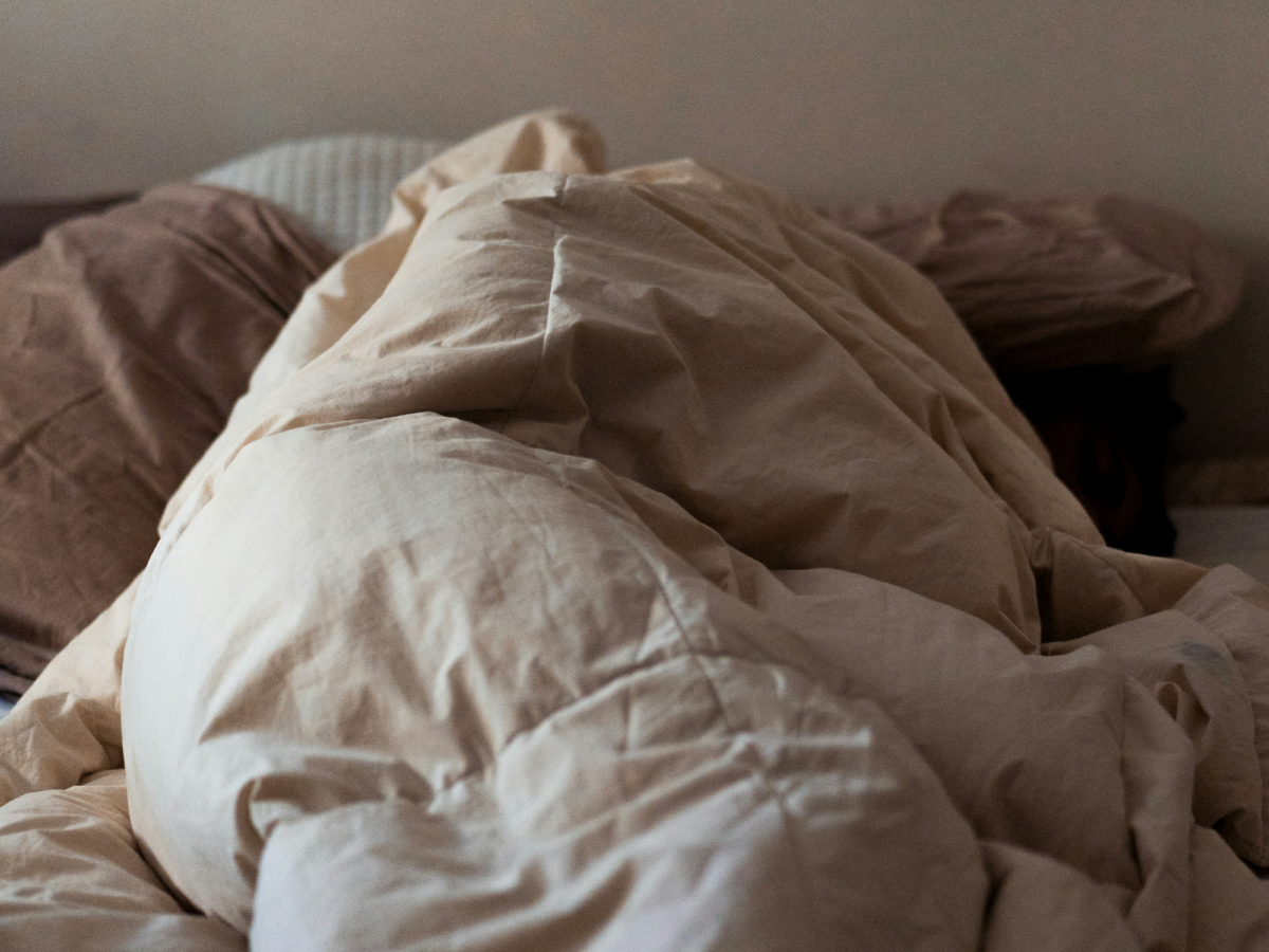 A person is wrapped in a comfortor in an unmade bed