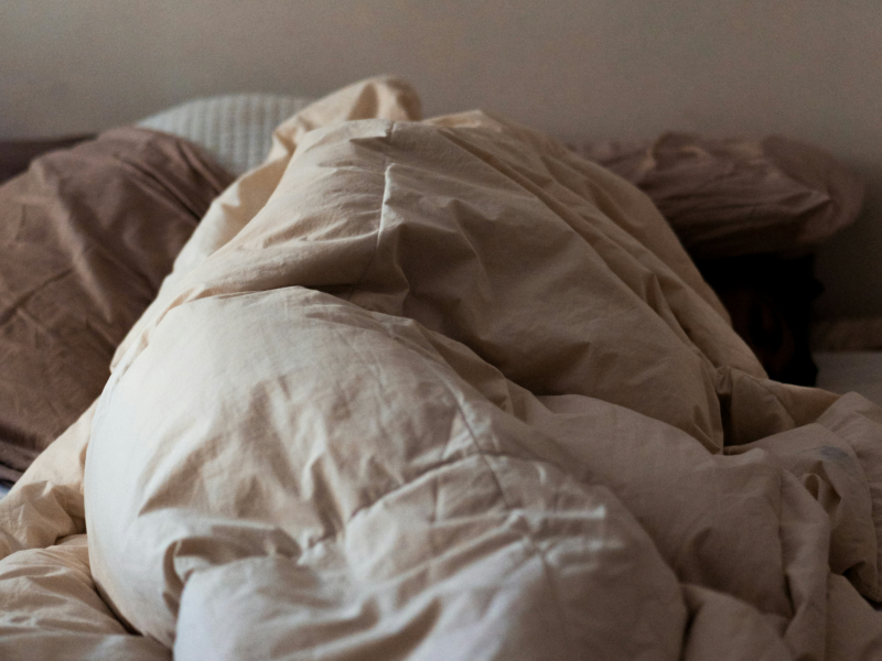 A person is wrapped in a comfortor in an unmade bed