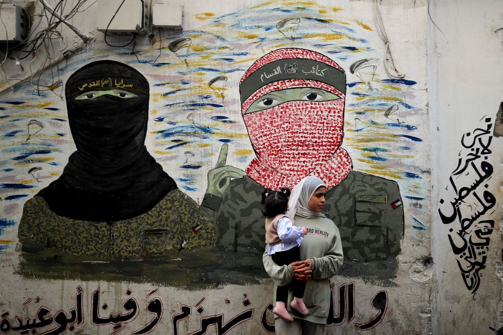 A woman stands in front of a graffiti of Hamas and Islamic Jihad spokespersons​