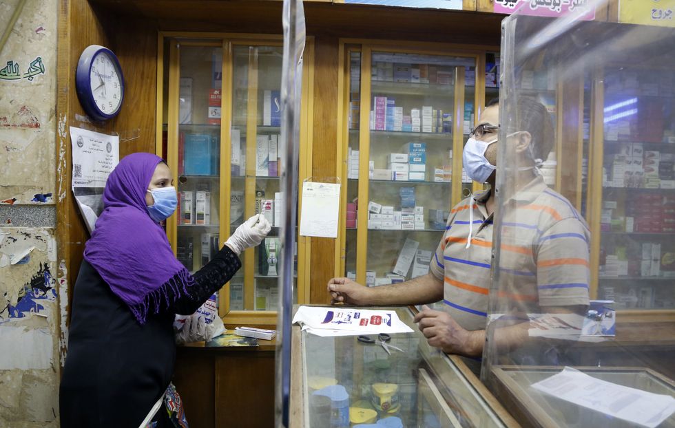 A woman wearing a face mask talks with a shop assistant at a pharmacy in Cairo, Egypt