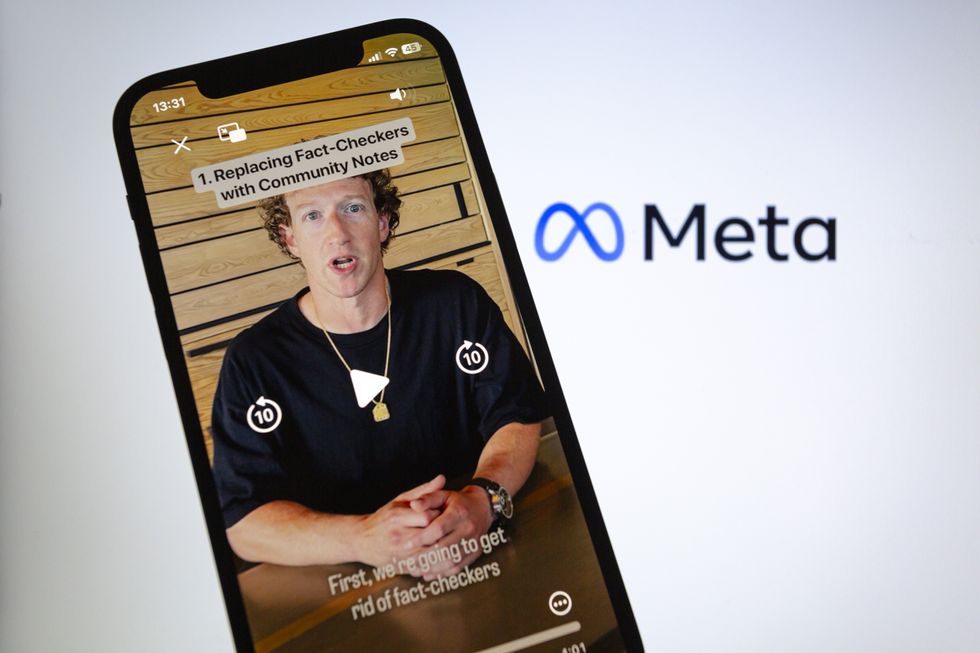 An iPhone with Mark Zuckerburg on it is in the foreground while a Meta sign is in the background