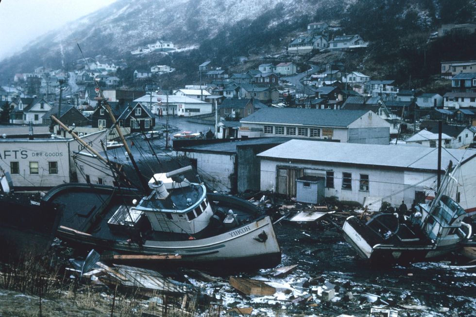 Image of wreckage on a port caused by a natural disaster, with remains of boats and houses floating on the surface of the water.