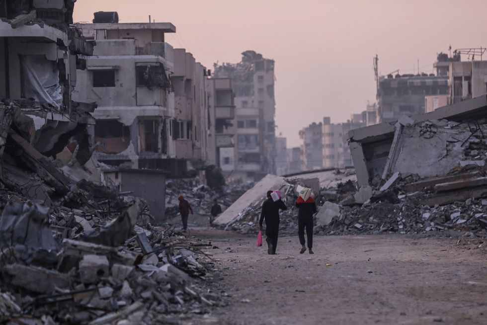 Palestinians walk among the rubble of destroyed buildings in the al-Rimal neighborhood of Gaza City
