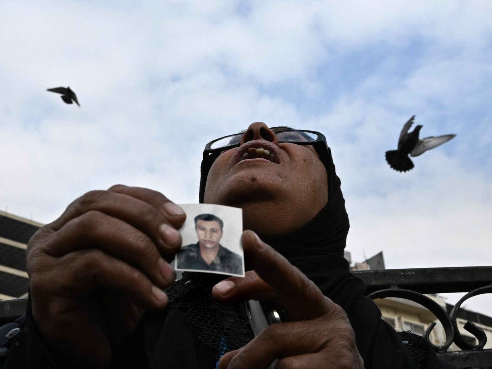 Photo of a woman holding a small picture of her son with birds flying