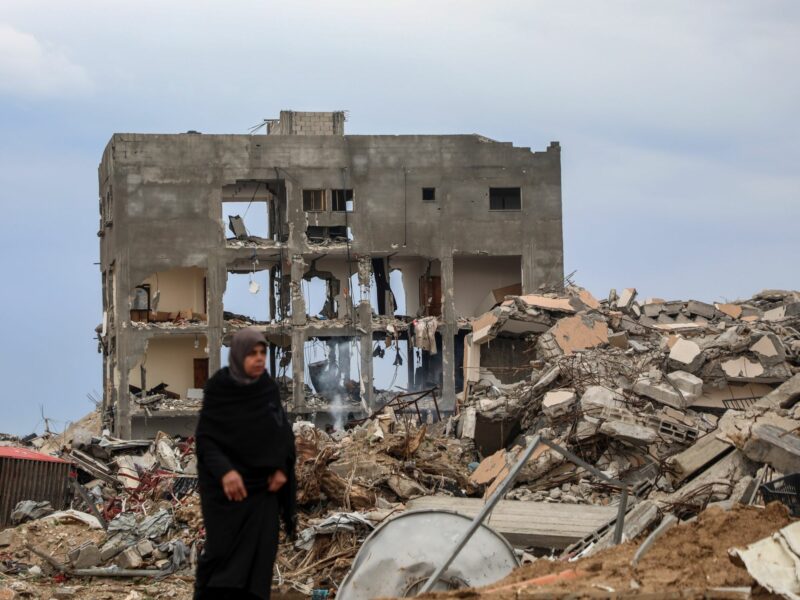 Photo of a woman walking past destroyed houses near the Netzarim Corridor in central Gaza, on Feb. 9.