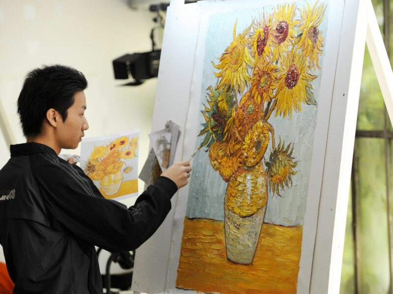 Photo of Chinese copyist Lu Hui, from Dafen, copying a sunflower painting by Dutch master Vincent Van Gogh