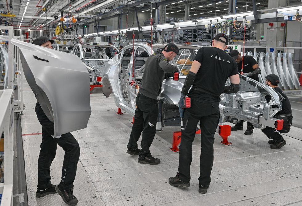 Photo of employees of the Tesla Gigafactory Berlin Brandenburg working on a production line of a Model Y electric vehicle.