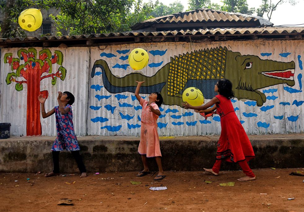 Village kids play with balloons beside a decorated Wall.