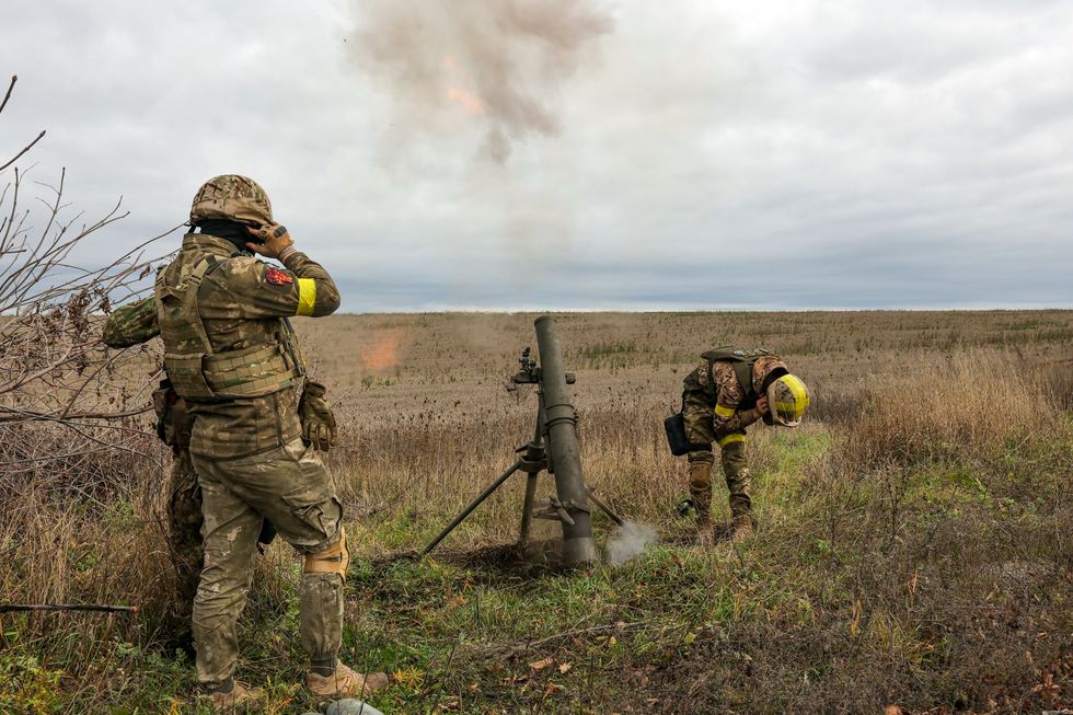 3 Ukraine soldier covering their ears as they fire mortar shells in a dry open field.