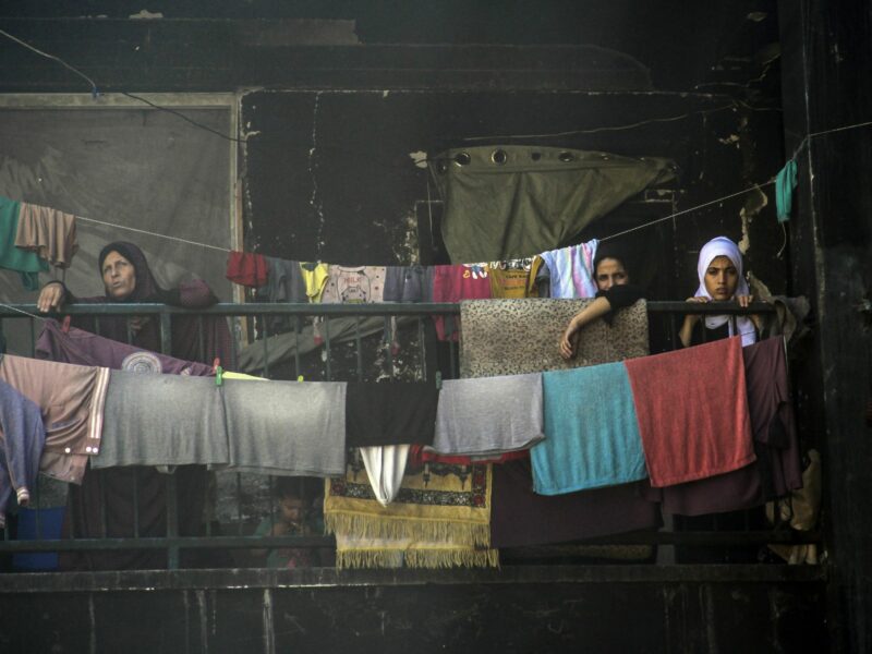 4 women standing on a balcony in between cloths and carpets hanging on clothe lines