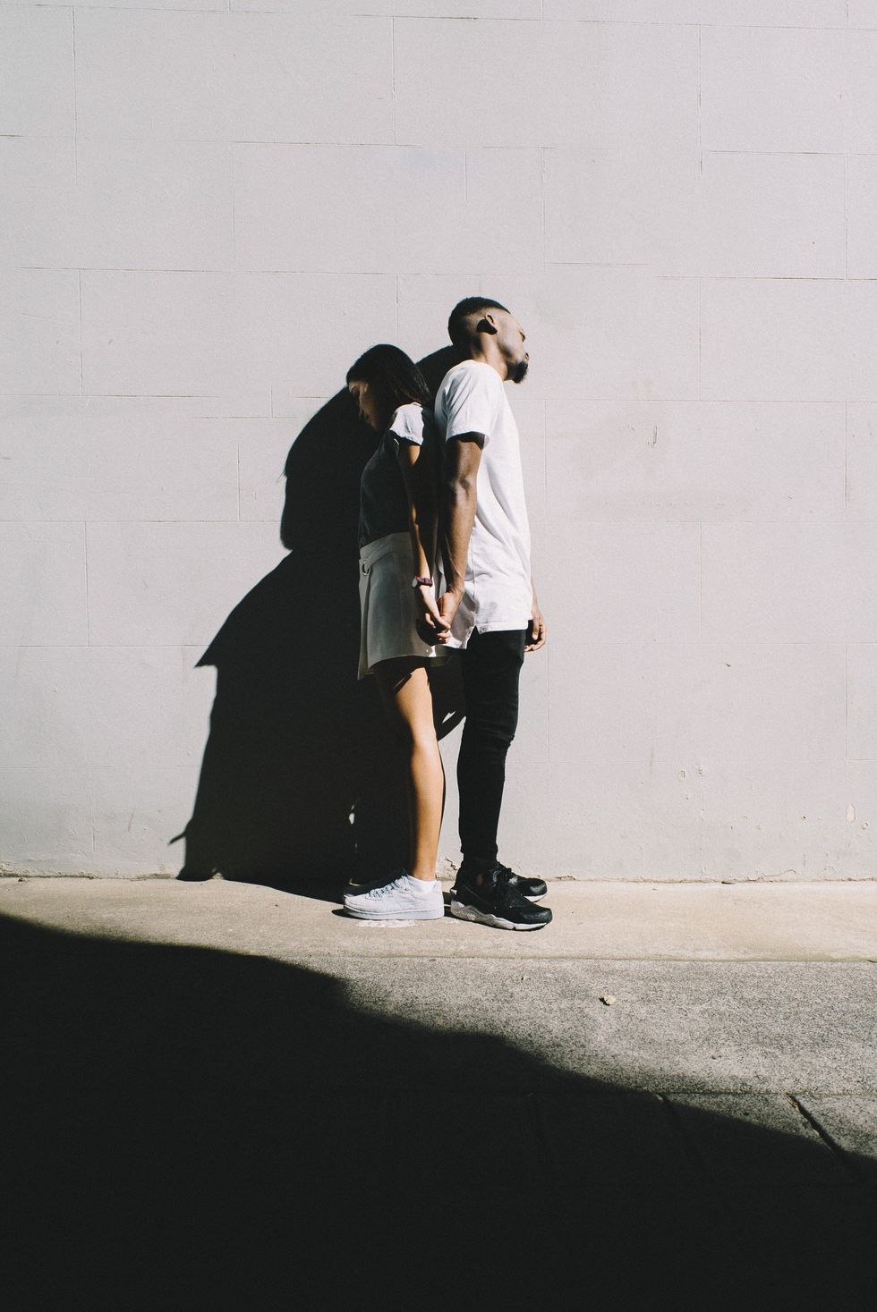A back-to-back couple leaning against a wall.