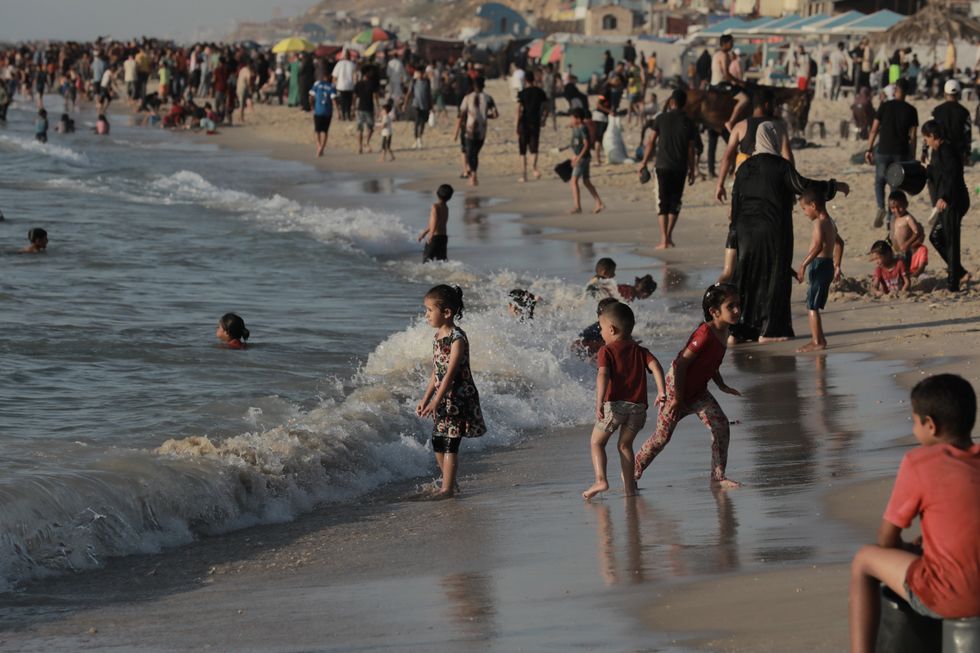 A beach scene with many children, enjoying the water as a small wave flows in