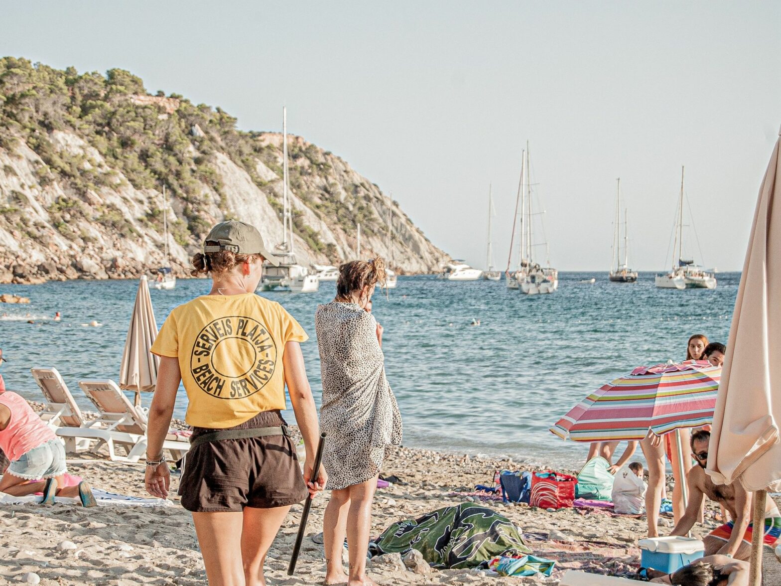 A beach services worker walks along the beach behind holidaymakers.