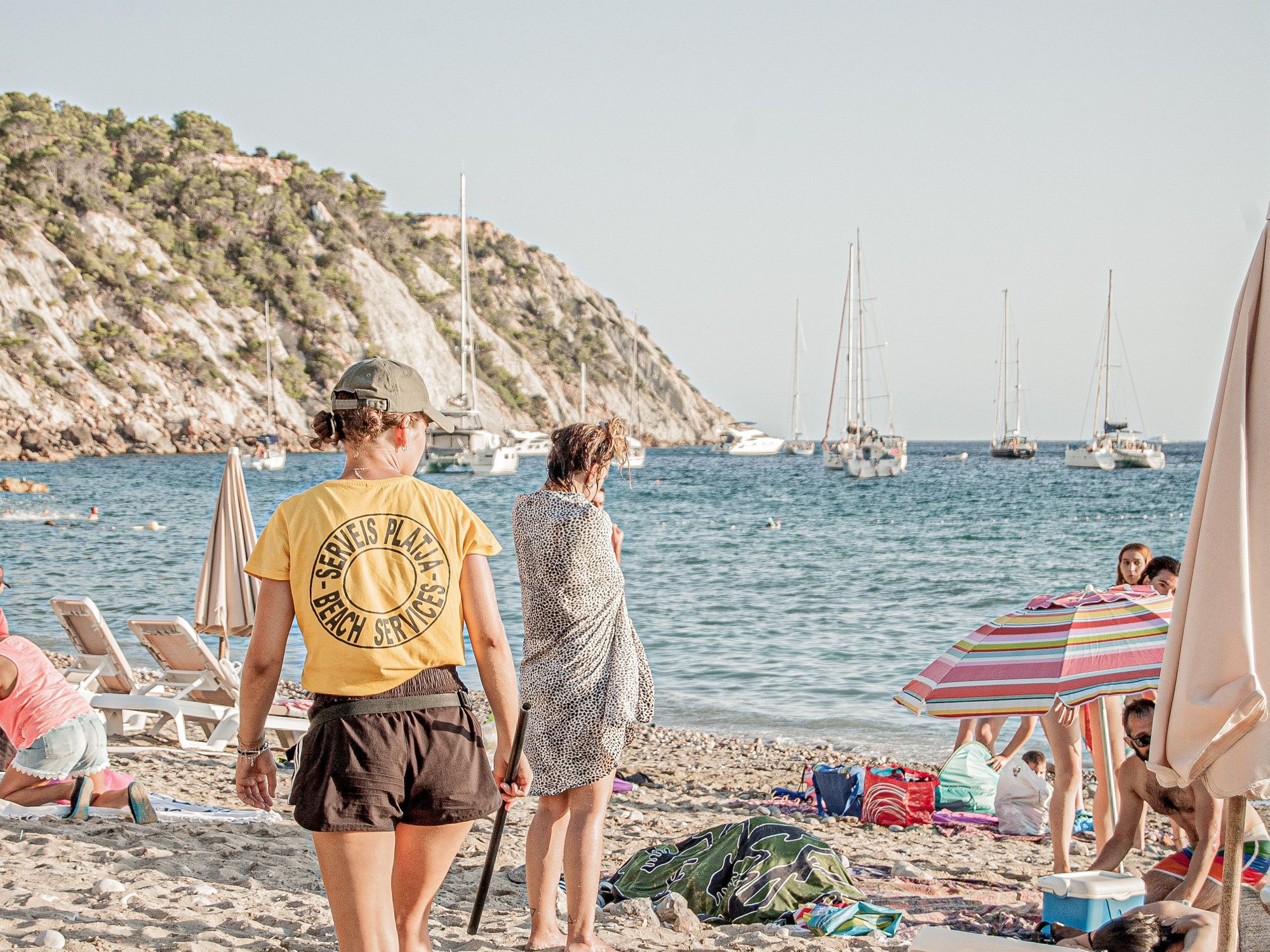 A beach services worker walks along the beach behind holidaymakers.