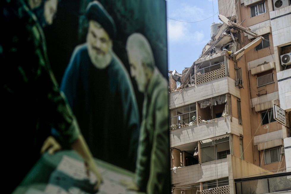 A billboard depicting pro-Iranian Hezbollah chief Hassan Nasrallah (C) with assassinated Iranian commander of al-Quds Brigade Qasem Soleimani (R) and assassinated Hezbollah top commander Imad Mughniyeh stands next to a destroyed building targeted by an Israeli drone in Beirut's southern suburbs in July 2024.