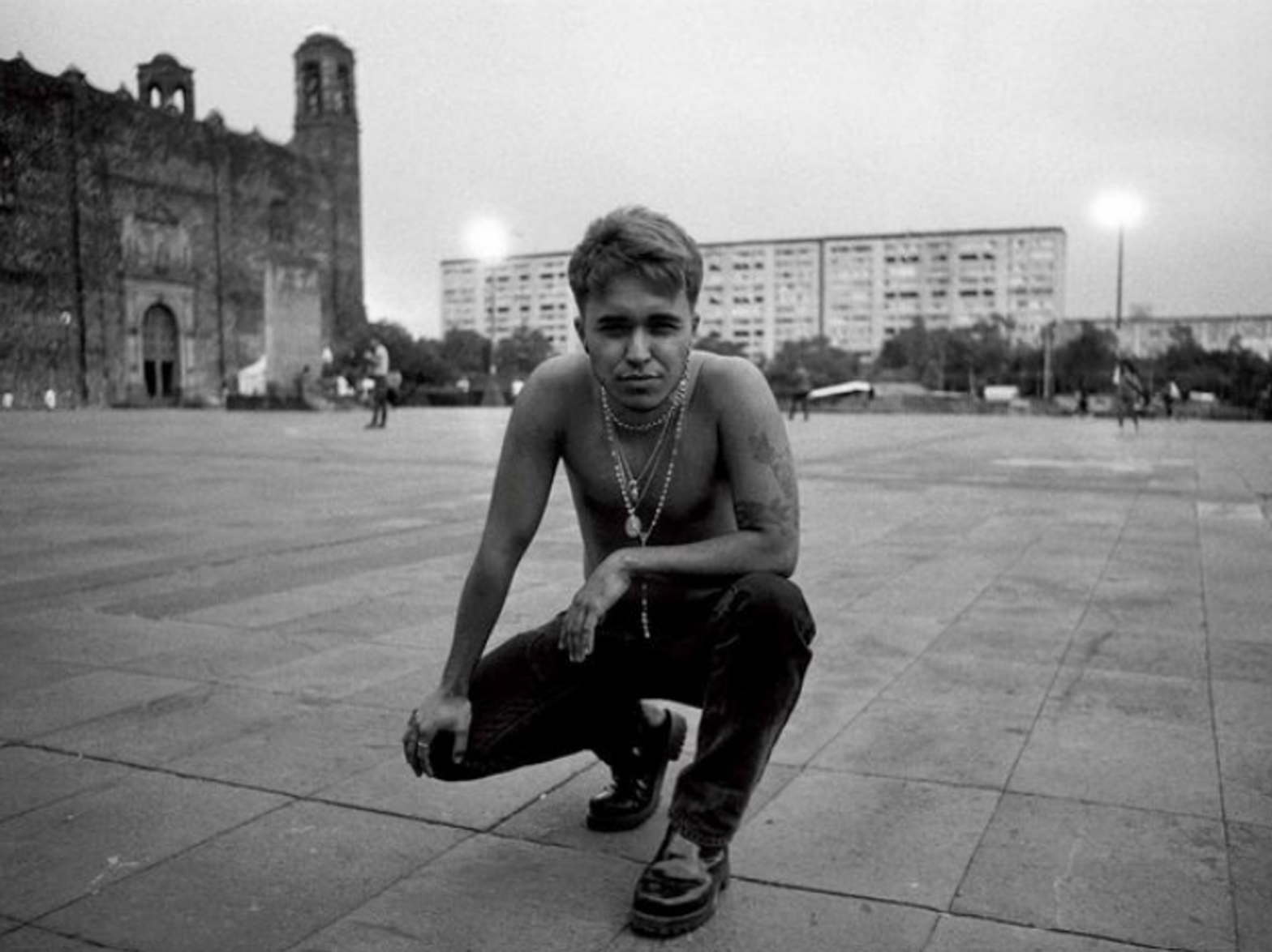 A black and white image of Dante Ureta kneeling on a plaza, shirtless, in Tlatelolco, Mexico City