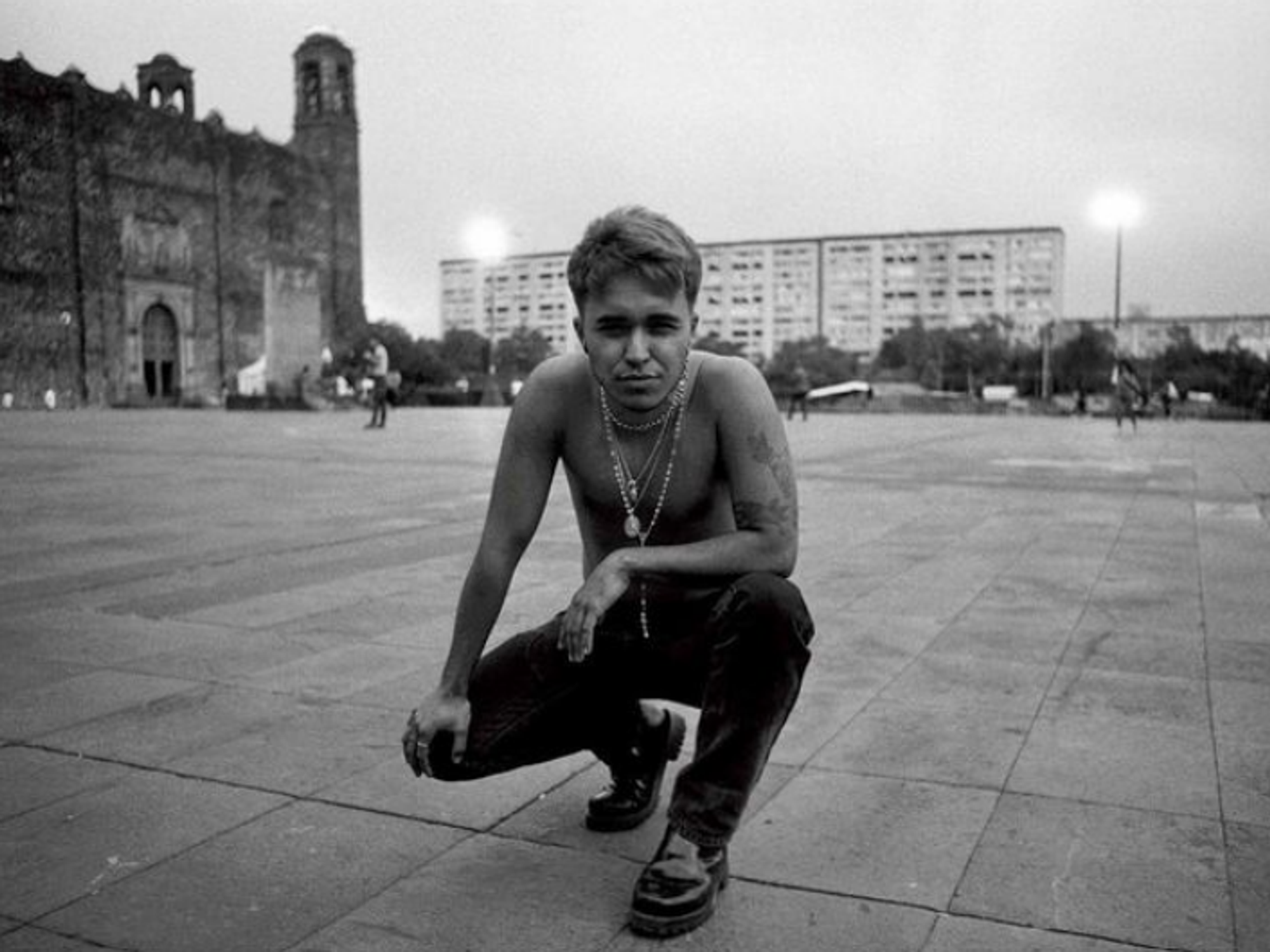 A black and white image of Dante Ureta kneeling on a plaza, shirtless, in Tlatelolco, Mexico City