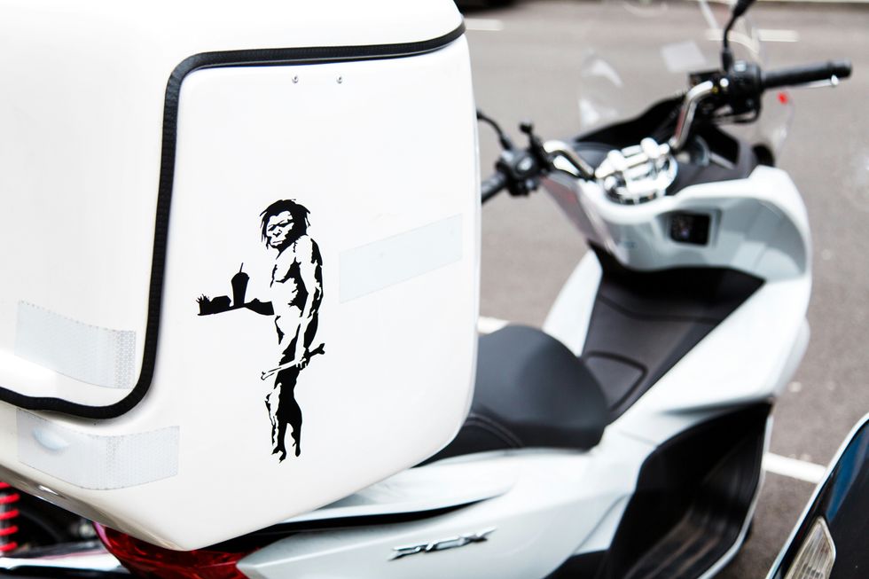 A black and white motor scooter with a caveman severing french fries.
