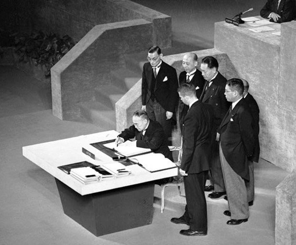 A black and white photo of Japanese diplomats in a grand hall signing an agreement