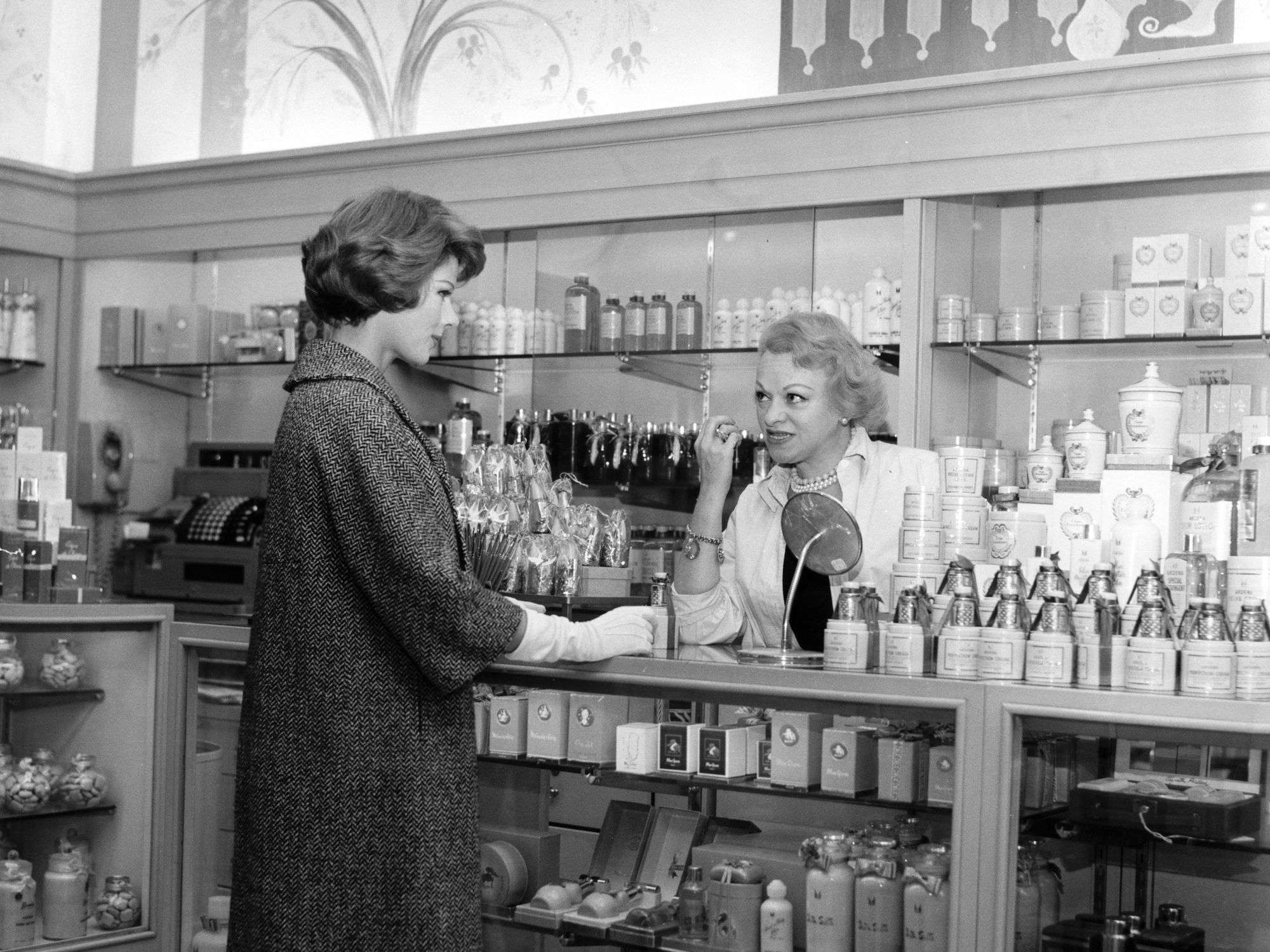 A black and white photo shows a perfume shop assistant advising a customer
