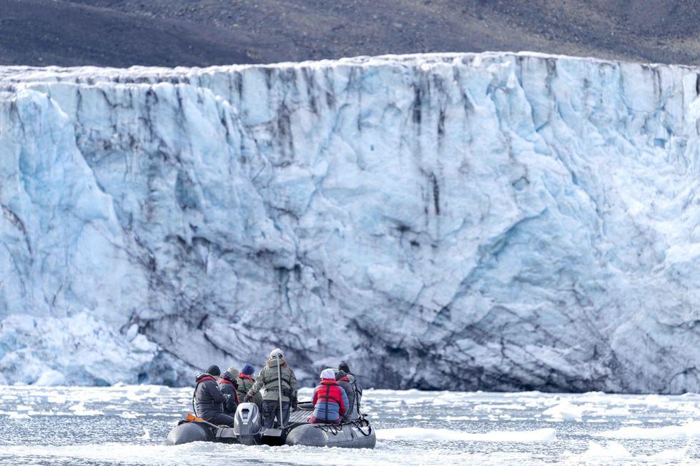 A boat with seven people in icy water heading towards a giant glacier