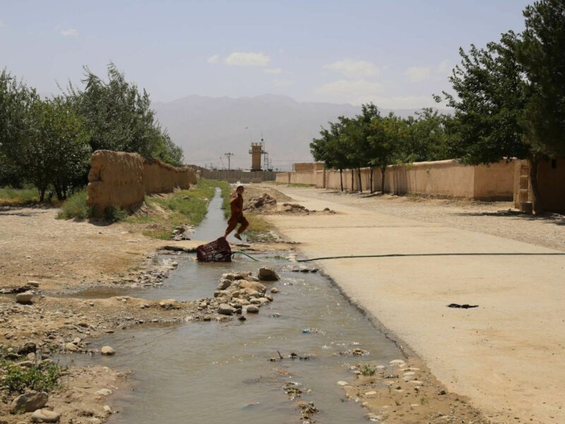 A boy jumps over a stream that flows out of the walls of the Bagram base. Several burn pit locations at the base, which studies have shown polluted the air far above EPA standards, were last active in mid-June of 2021.