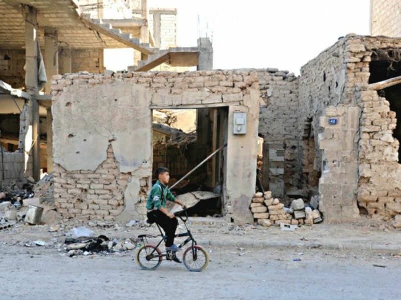 A boy rides a bicycle amid rubble in Homs