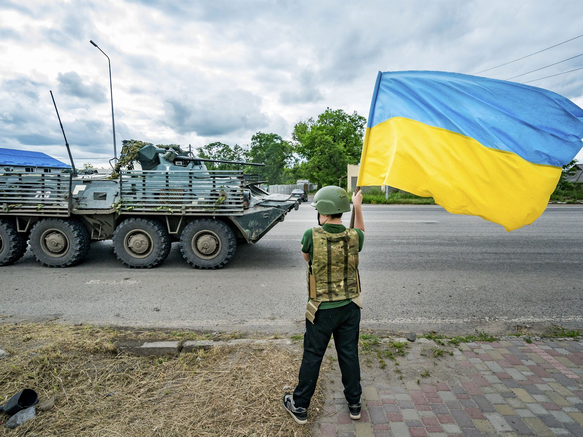 A boy waves a Ukrainian flag as a Ukrainian armored vehicle drives by