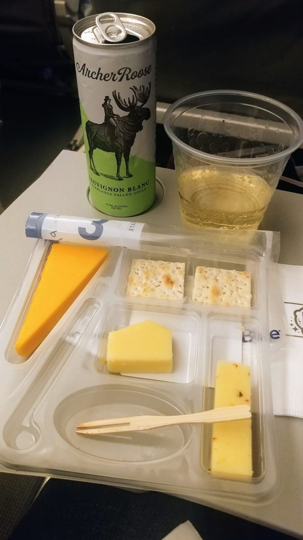 A can of Sauvignon white wine with a cheese and crackers platter in an airplane.