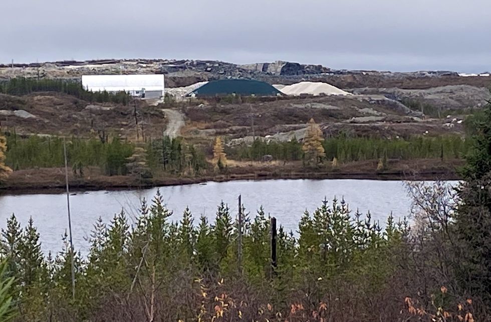 A Canadian mine is seen behind some trees and a stretch of water.