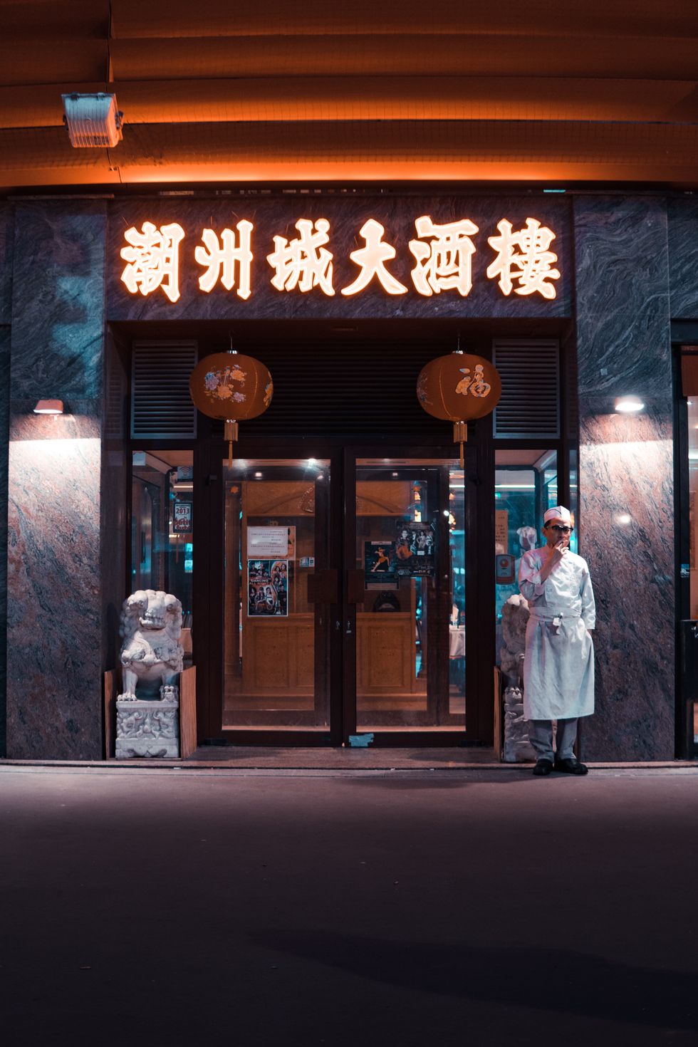 A chef stands smoking infront of a well lit Chinese restaurant