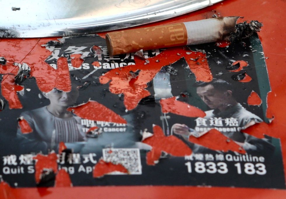 A cigarette bud is placed on a ripped up anti-smoking campaign sticker.