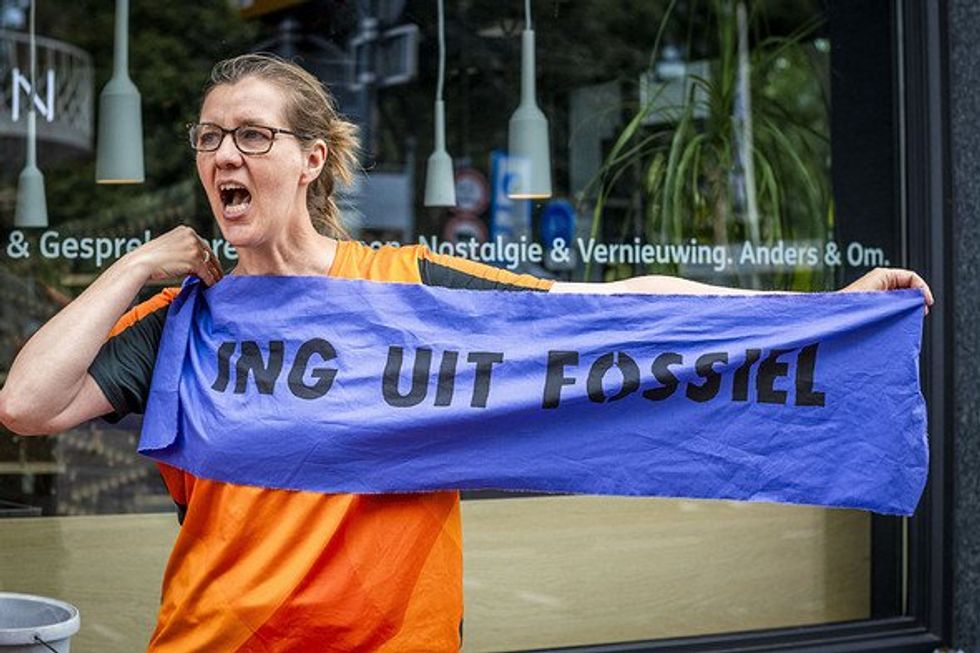 A climate activist holds a banner reading ''ING Uit Fossiel'' (ING Out of Fossil).