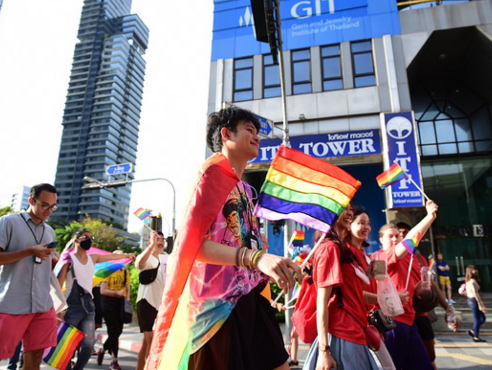A colorful LGBTQ protest taking place in Thailand, many people are gathered wearing colorful clothes and waving flags