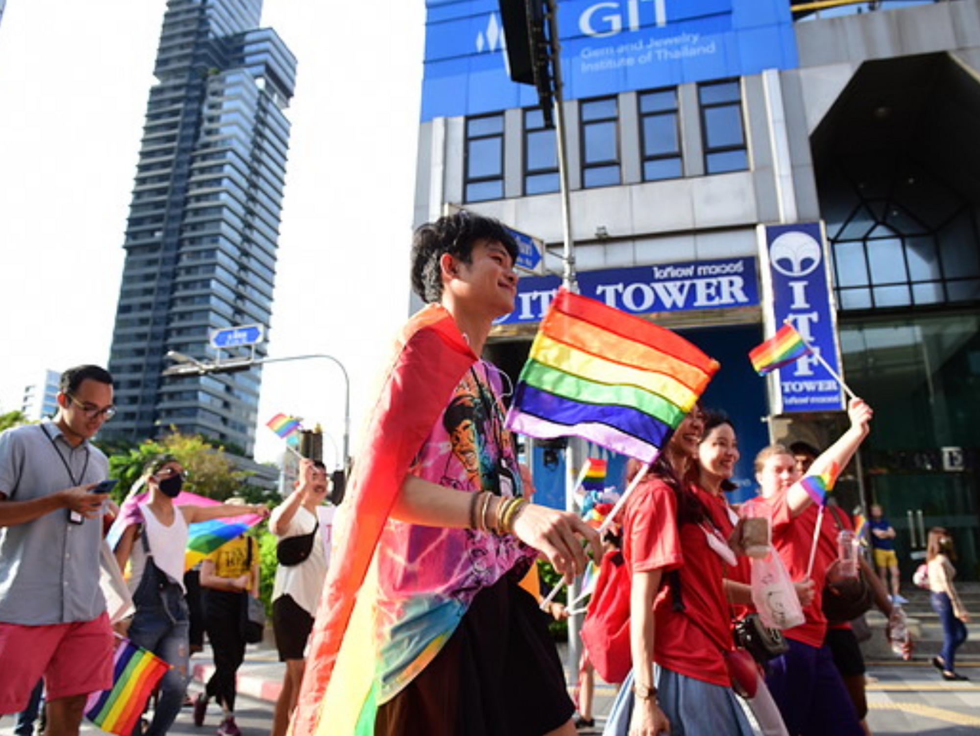 A colorful LGBTQ protest taking place in Thailand, many people are gathered wearing colorful clothes and waving flags