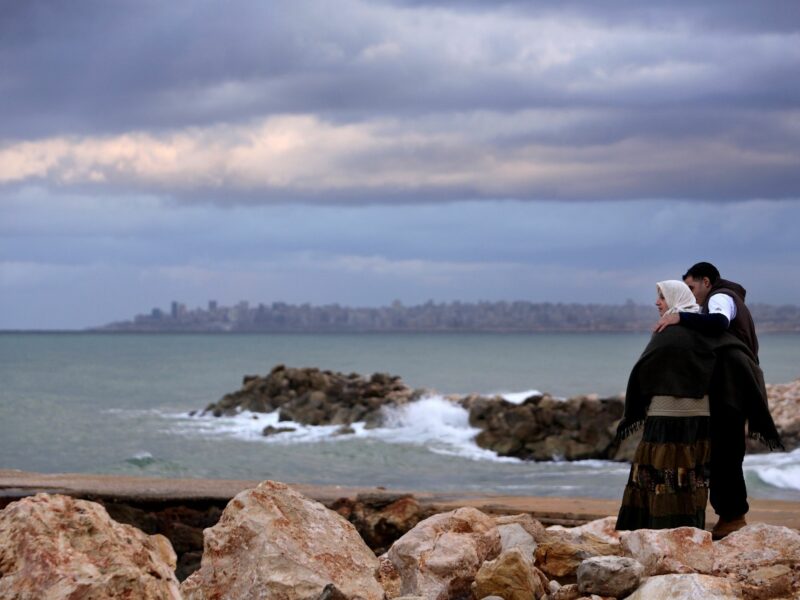 A couple looking at the sea at sunset. In the distance, the city of Beirut. Sidon, Lebanon.