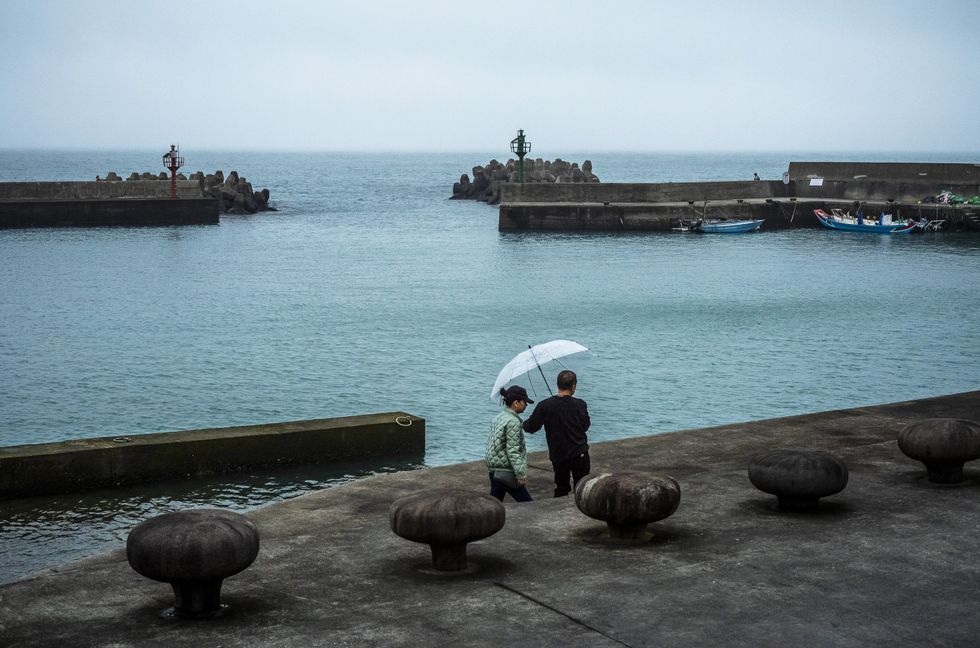A couple with an umbrella walks along the fisherman harbour on the coastline.