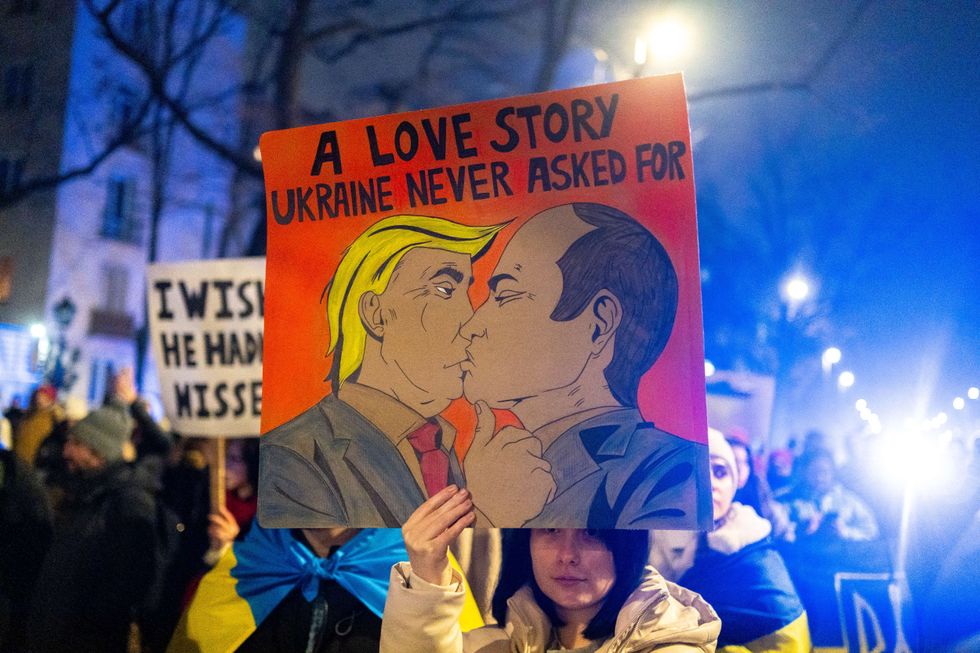 A demonstrator holds a sign of Trump and Putin kissing, with the caption "A love story Ukraine never asked for", at a protest outside the Ukrainian embassy in Warsaw, on the third anniversary of Russia's invasion of Ukraine.