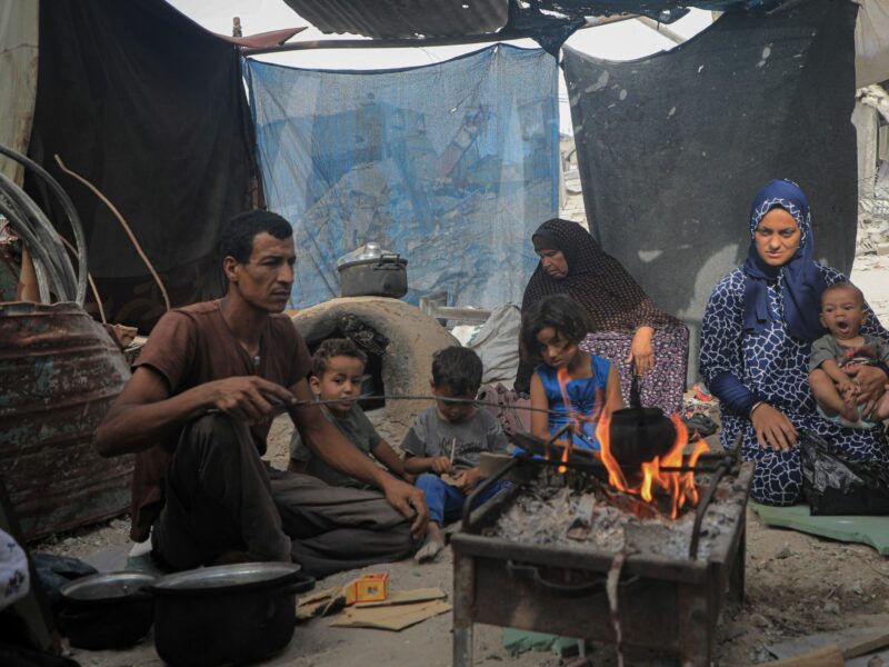 A family of 9 sitting in a tent surrounding a fire