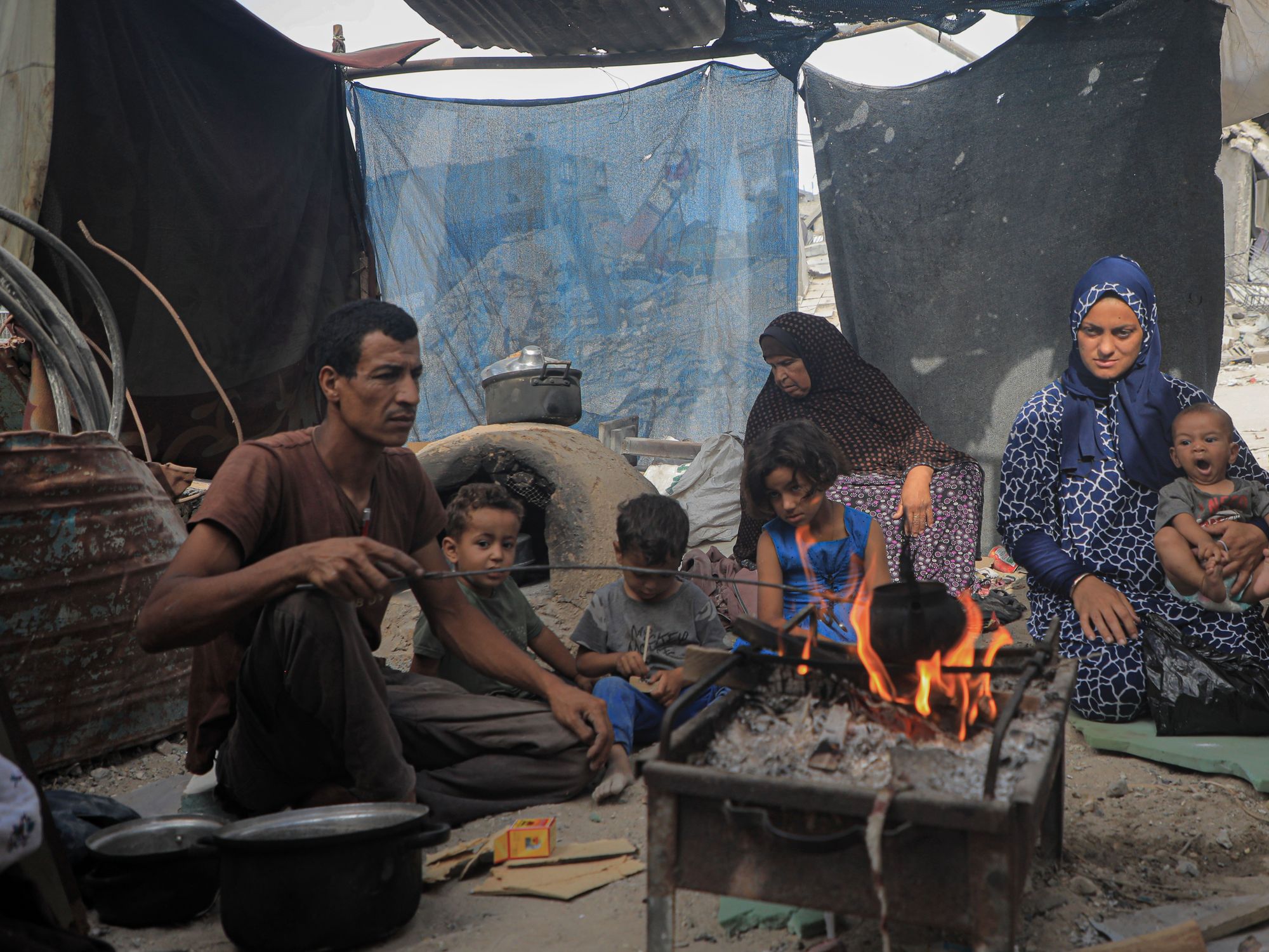 A family of 9 sitting in a tent surrounding a fire
