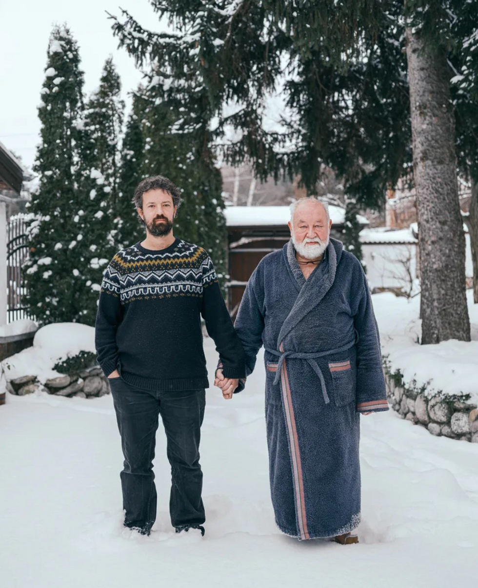 A father and his adult son stood holding hands in the snow.
