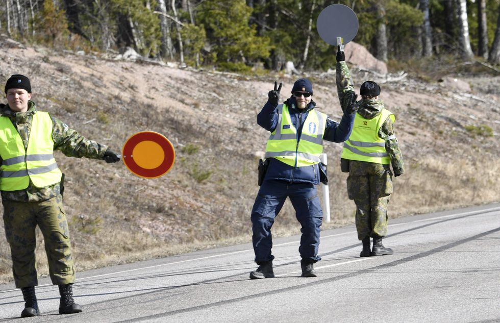 A Finnish policeman doing V hand signs and army conscrpits holding stop signs on a road at police checkpoint