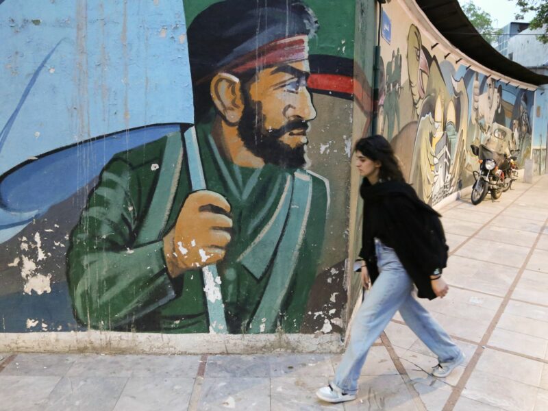 A girl walks past a large mural depicting a man holding a flag