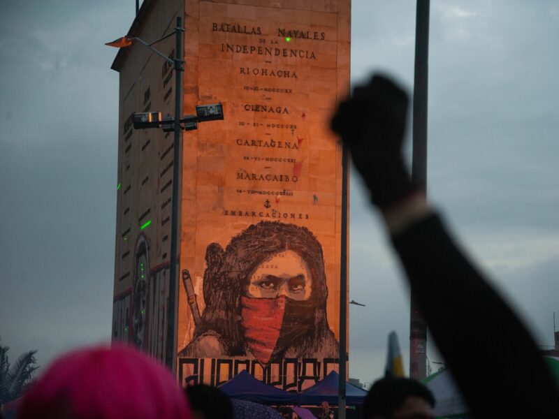 A gloved, raised fist contrasts against feminist artwork on a memorial monuement