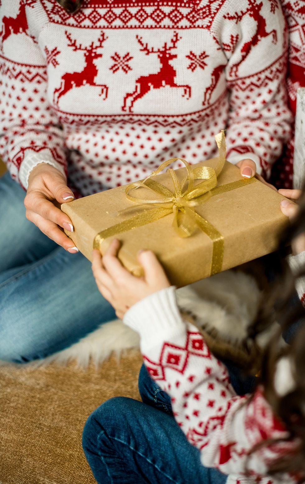 A golden wrapped gift being exchanged between two people. The gift is the focus of the shot.