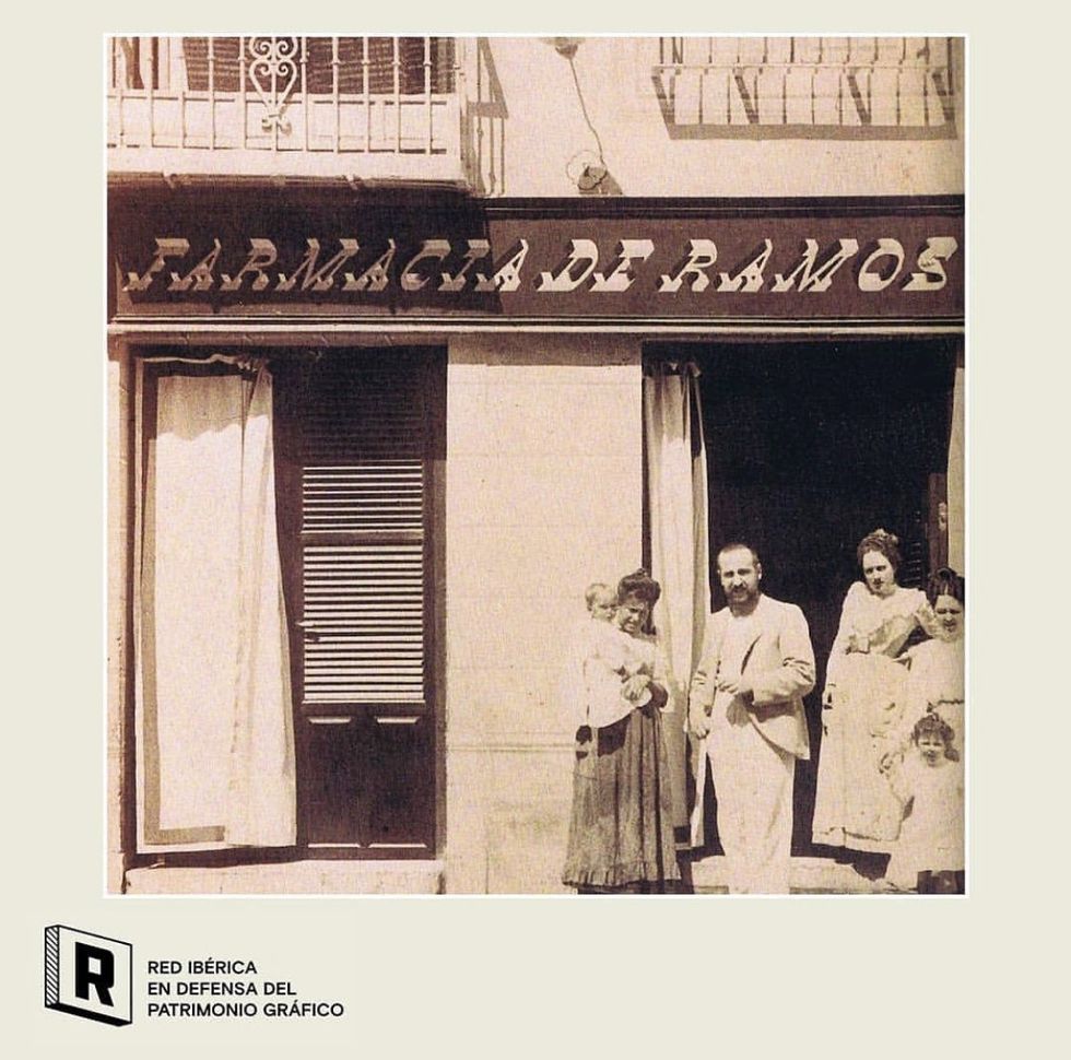 A greyscale photograph of a family infront of a building with a pharmacy sign